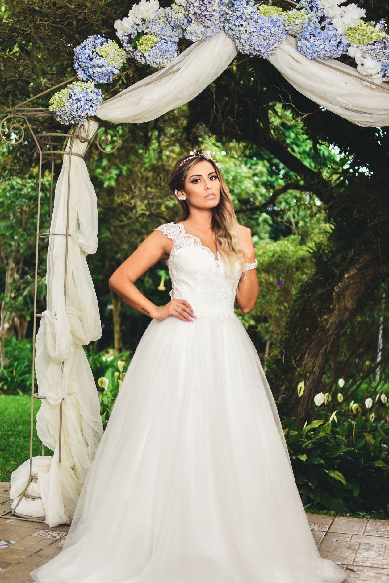 Novia con vestido de encaje bajo un arco de flores en un jardín frondoso