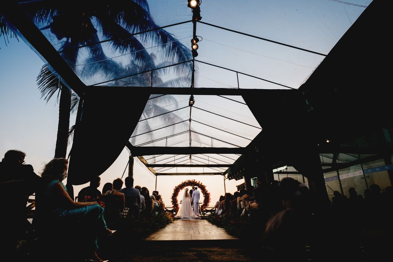 Ceremonia de boda al atardecer bajo una carpa de cristal con vegetación e invitados sentados